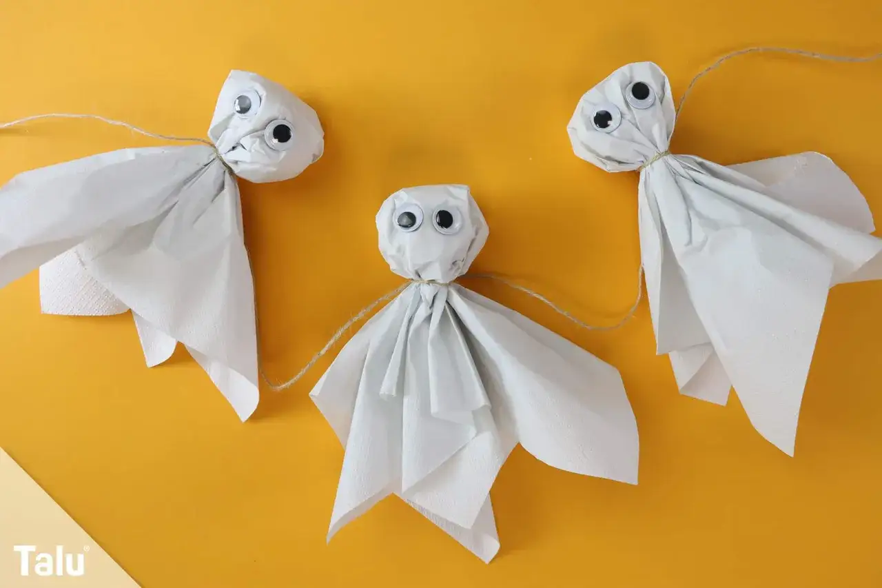 Drei süße Geister aus Papier mit Knopfaugen, die an einer Schnur hängen. Perfekt für gespenster basteln vorlagen.