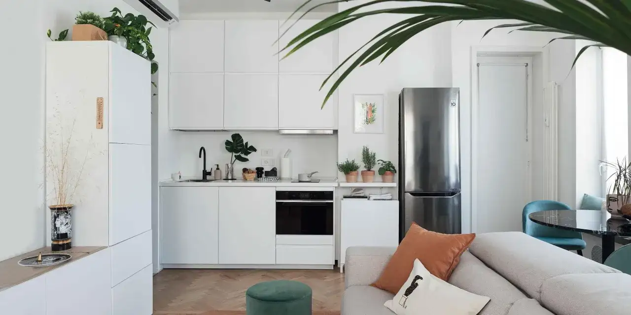 Interni moderni per un **progetto casa 55 mq rettangolare**: cucina bianca minimalista, frigorifero in acciaio, divano accogliente e piante verdi.