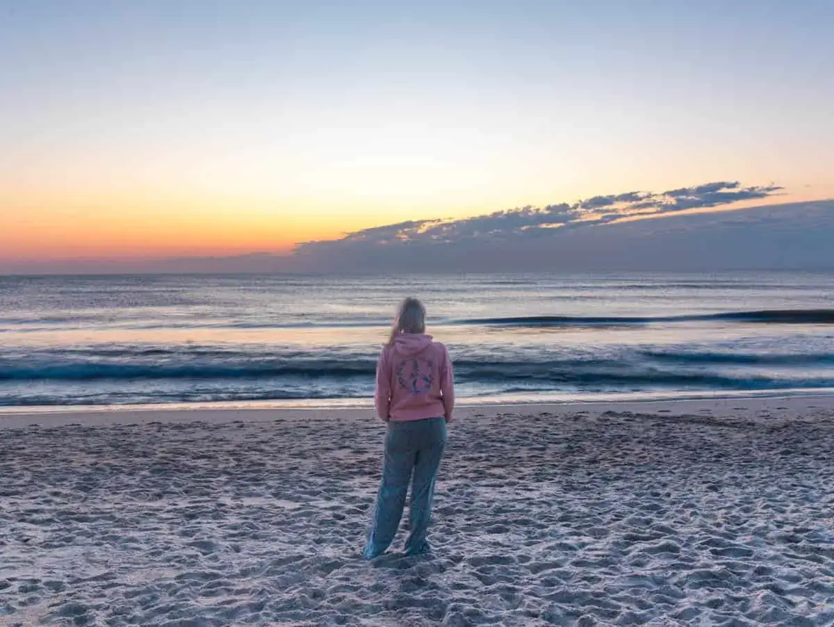 Mujer en la playa al amanecer, contemplando el mar azul y tranquilo.