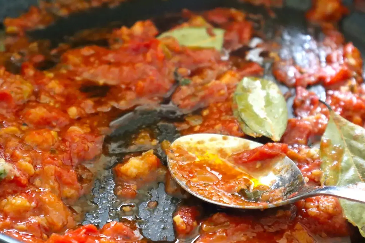 Ein Löffel voller köstlicher, langsam gekochter San Marzano Tomaten mit Lorbeerblättern in einer Pfanne.