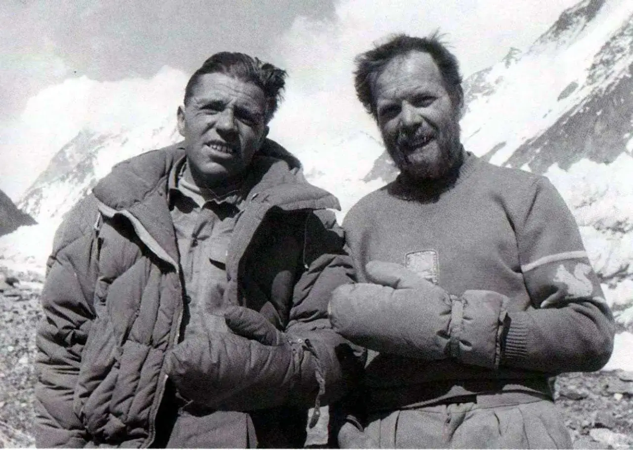 Zwei Bergsteiger, die die K2-Erstbesteigung feierten, posieren vor schneebedeckten Gipfeln.