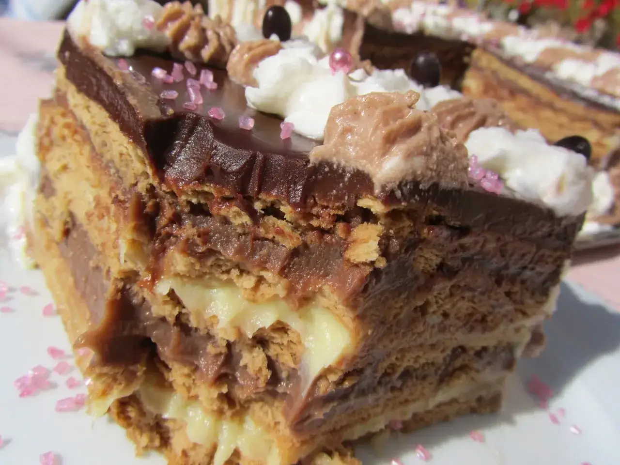Tarta de la abuela Thermomix: capas de galleta, crema pastelera y chocolate, decorada con nata y virutas rosas. &iexcl;Un postre casero irresistible!