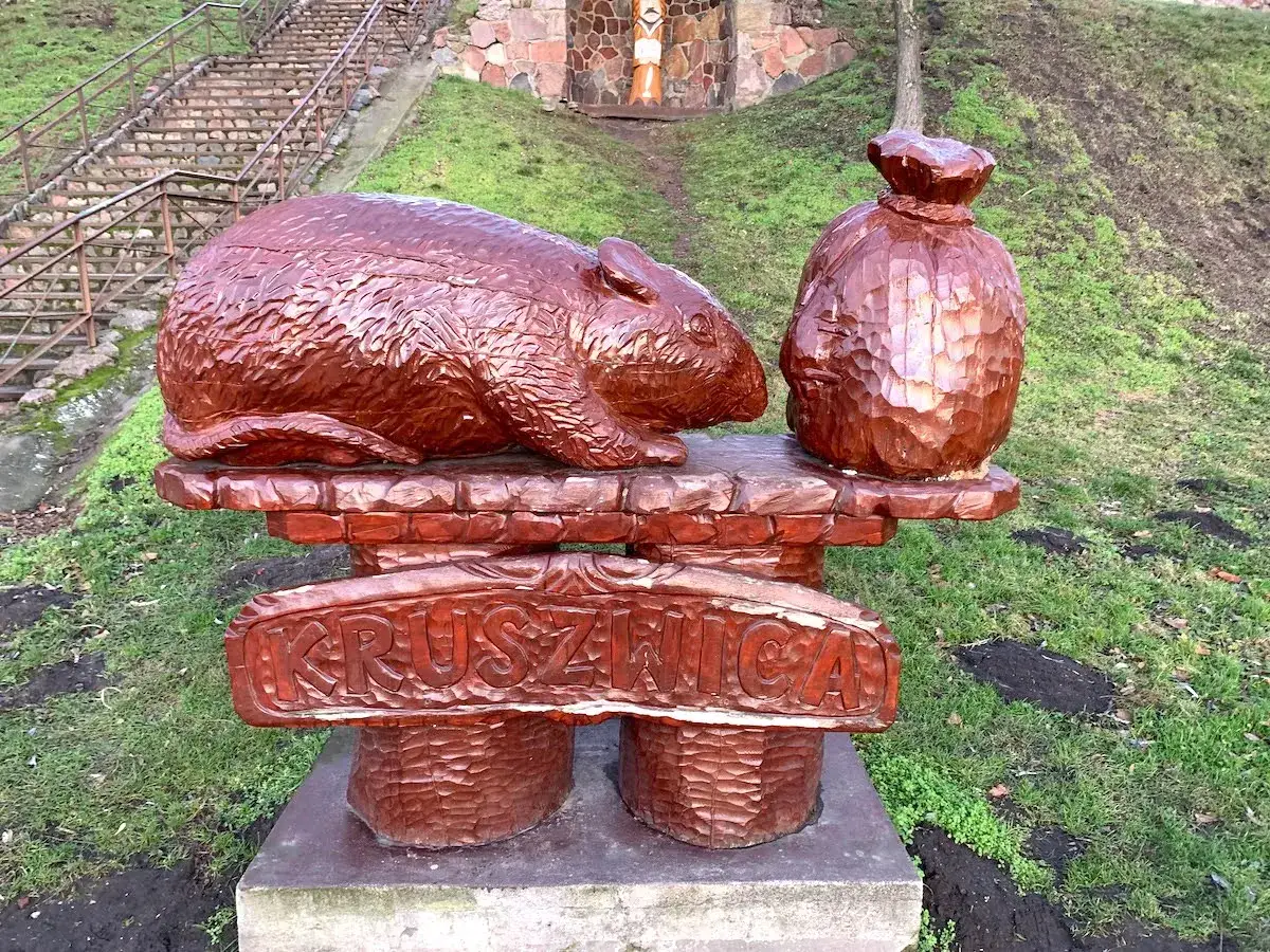 Drewniana rzeźba szczura i worka, nawiązująca do baśni o Popielu. Podpis