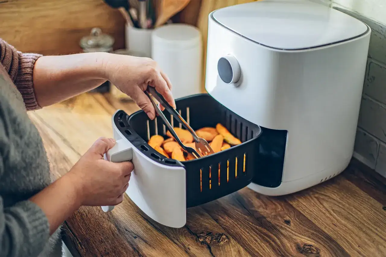 Ręka wkłada frytki do frytkownicy beztłuszczowej. Tak działa air fryer, szybko i zdrowo przygotowując posiłki.