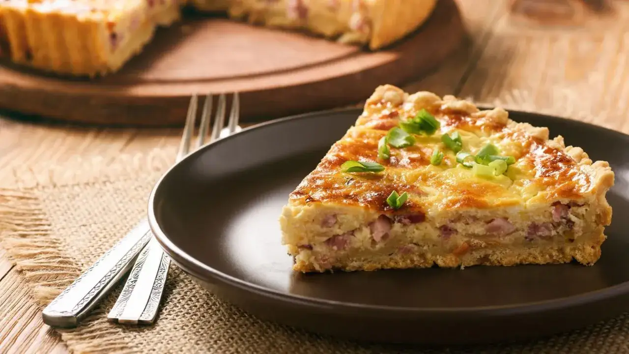 Une part de quiche lorraine épaisse et moelleuse, garnie de ciboule fraîche, sur une assiette brune.