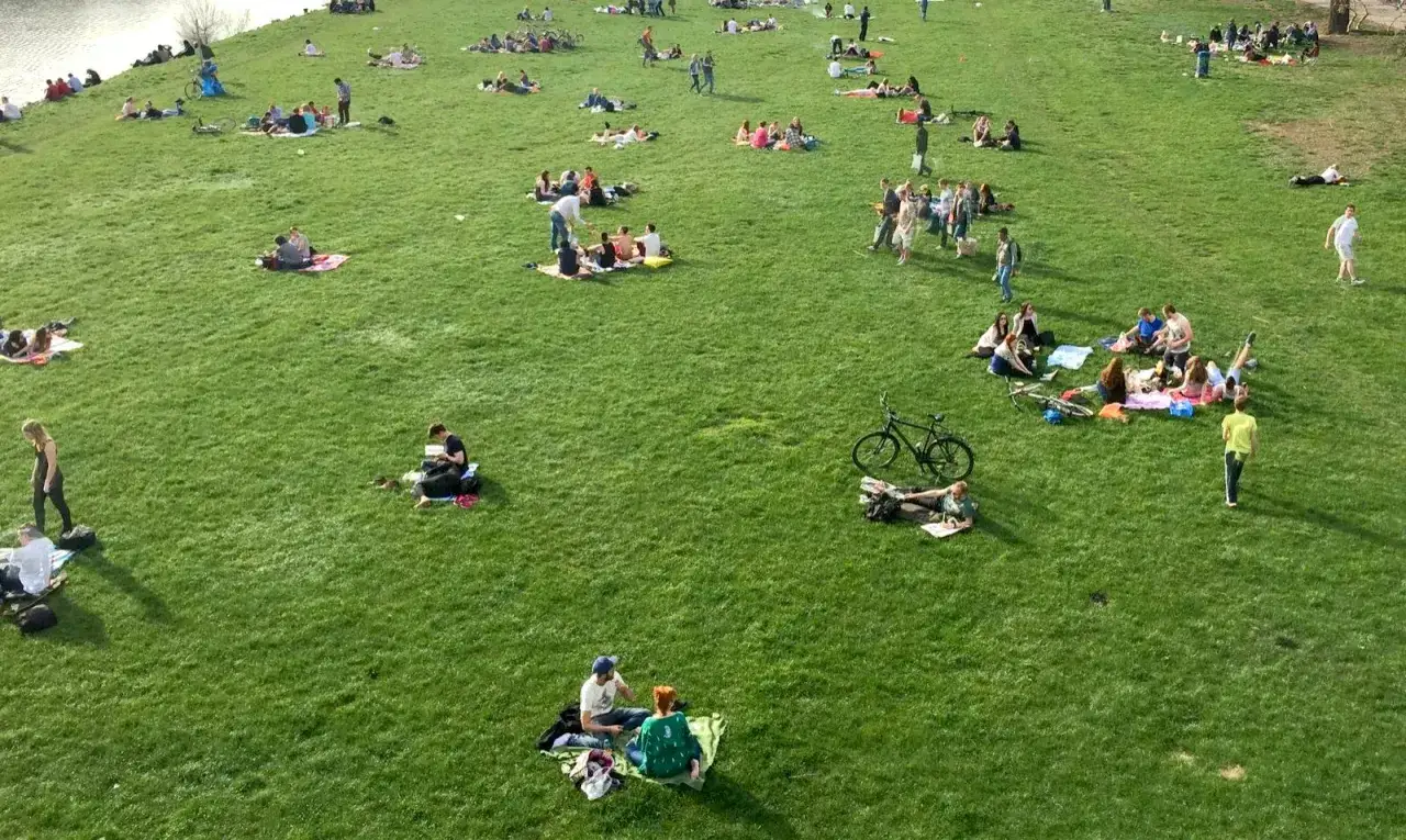 Menschen genie&szlig;en das sonnige Wetter auf der Neckarwiese Mannheim. Viele liegen auf Decken, picknicken oder entspannen sich im Gras.