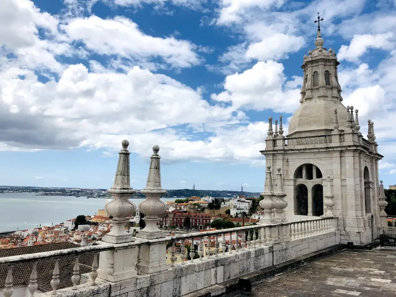 Blick von einer Dachterrasse auf Lissabon mit Blick auf den Tejo und die Stadt. Ein Kirchturm ragt empor. Perfekt für Lissabon Geheimtipps.