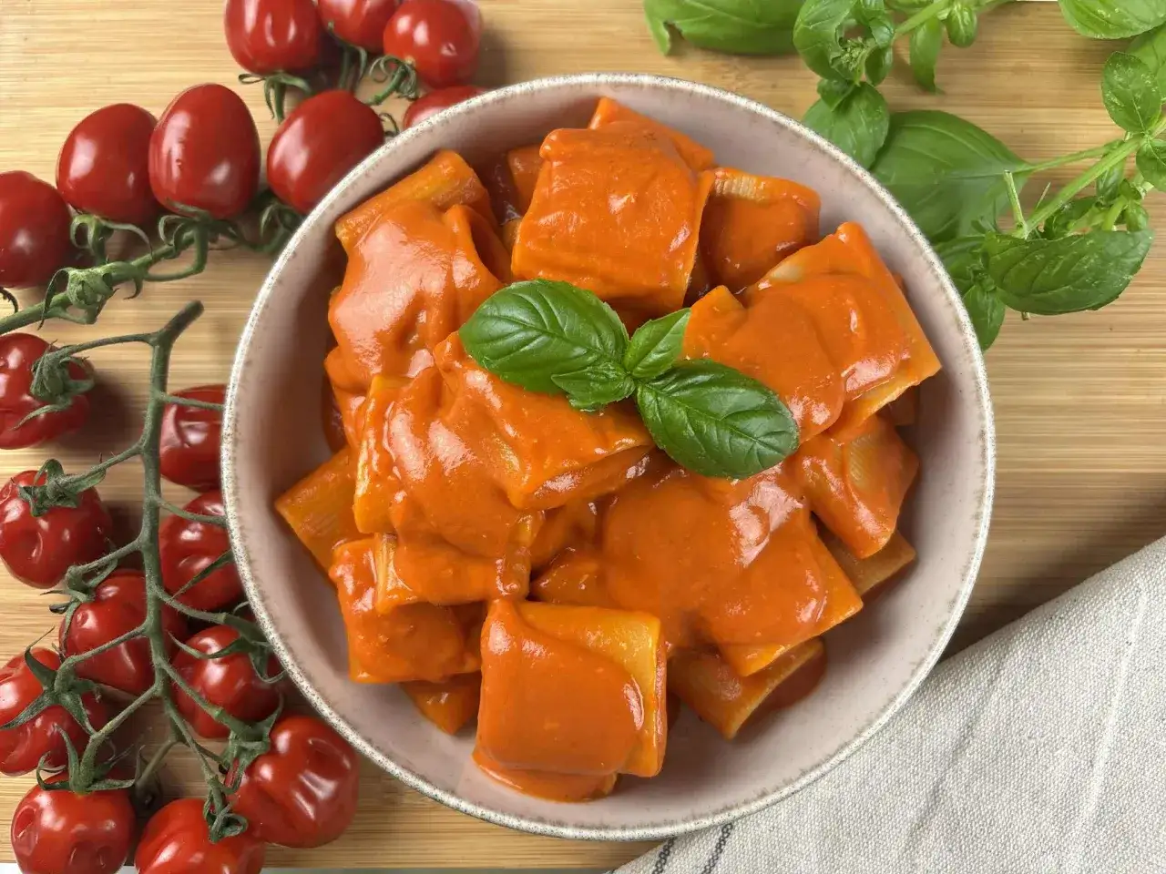 Un piatto di paccheri alla Vittorio, conditi con una ricca salsa al pomodoro e guarniti con basilico fresco, accanto a pomodorini maturi.