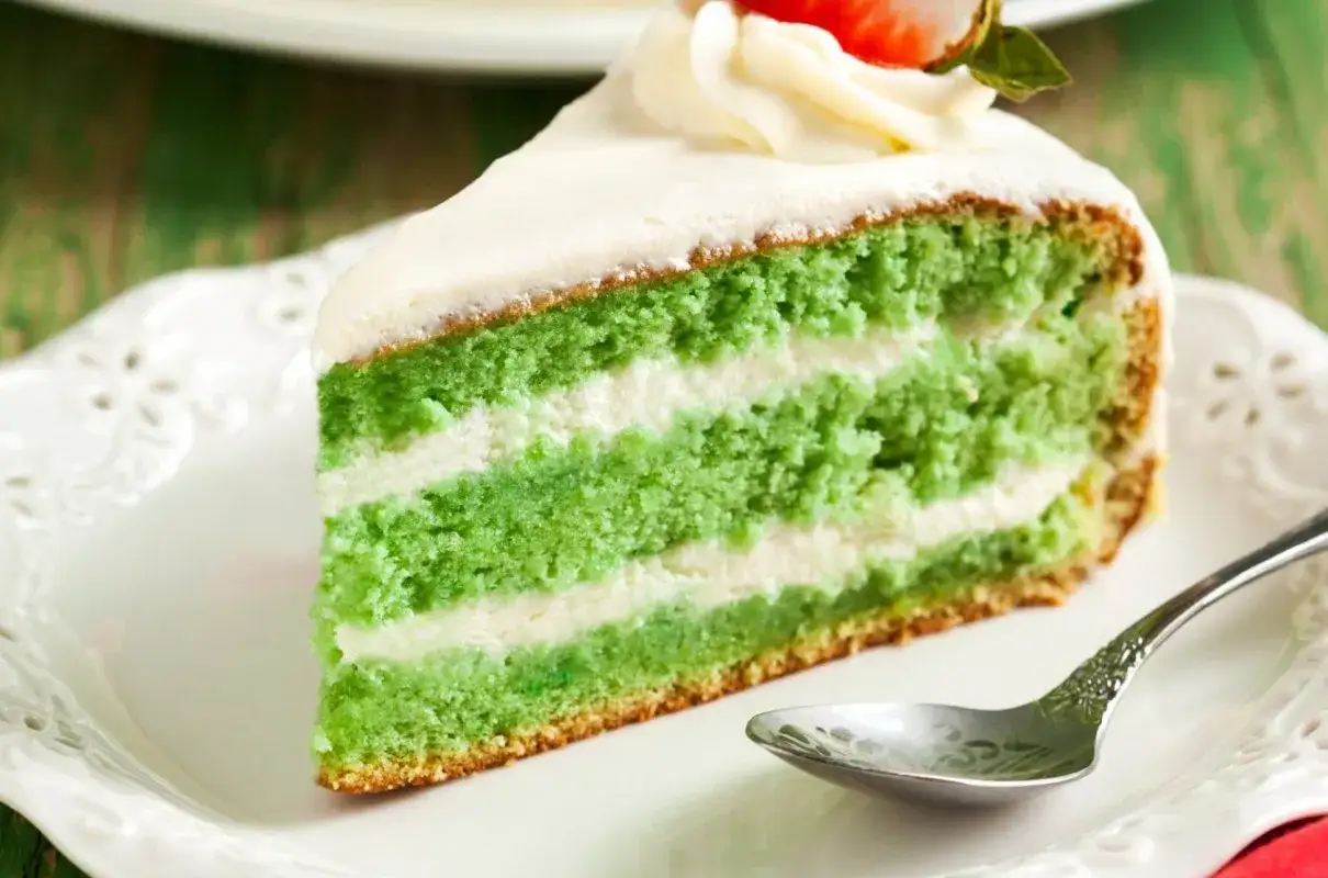 Zielony, warstwowy deser z kremem. To pyszne ciasto z matcha i mascarpone, udekorowane bitą śmietaną i truskawką.