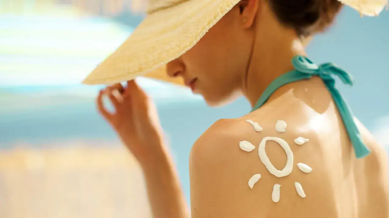 Une femme porte un chapeau de paille et de la crème solaire en forme de soleil sur son épaule. Est-ce que la crème solaire empêche de bronzer ?