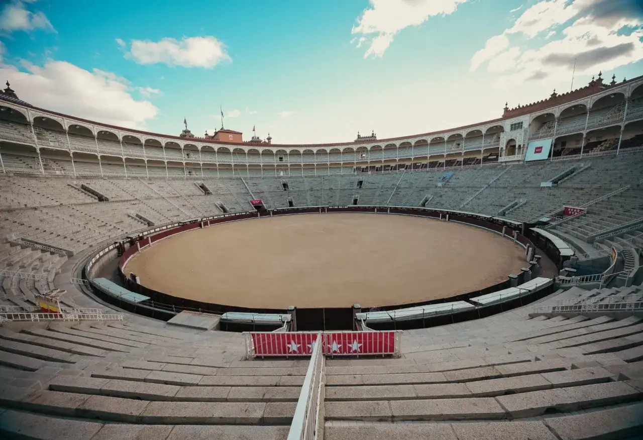 La plaza de toros de Madrid, vacía bajo un cielo azul con nubes, espera la emoción.