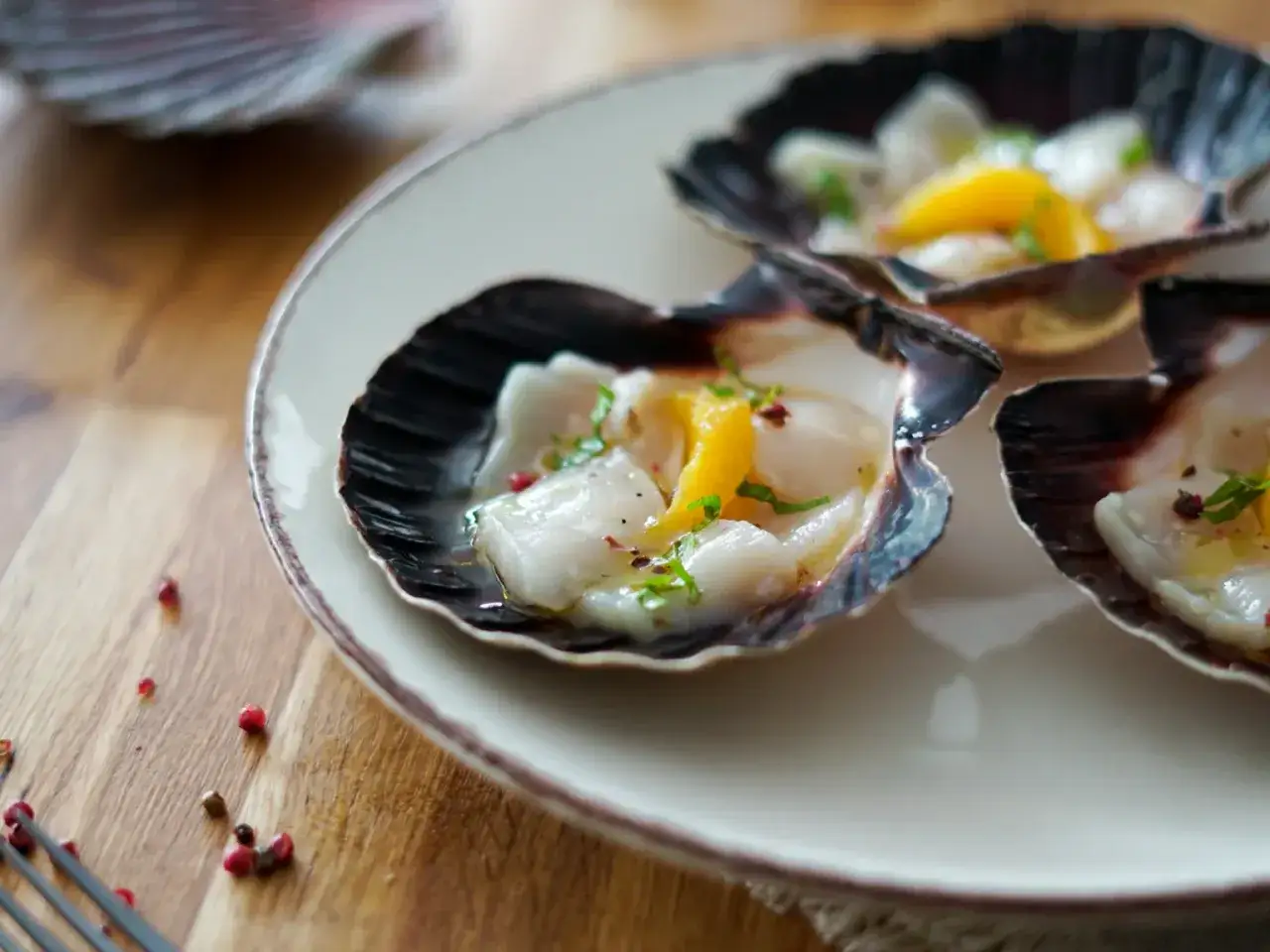 Saint-Jacques crues, zestes d'agrumes et herbes fra&icirc;ches dans leur coquille. Une recette entr&eacute;e originale et raffin&eacute;e pour un repas d'exception.