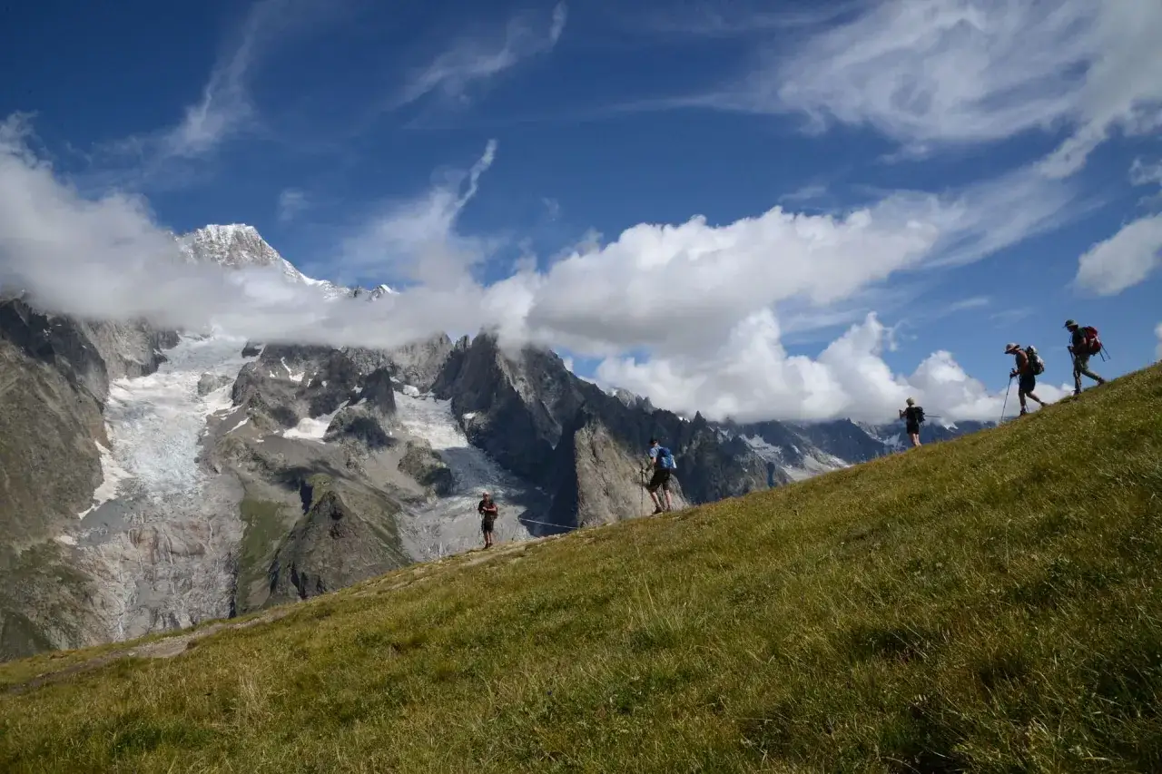 Escursionisti su sentieri Valle d'Aosta, con maestose montagne innevate e ghiacciai sullo sfondo.