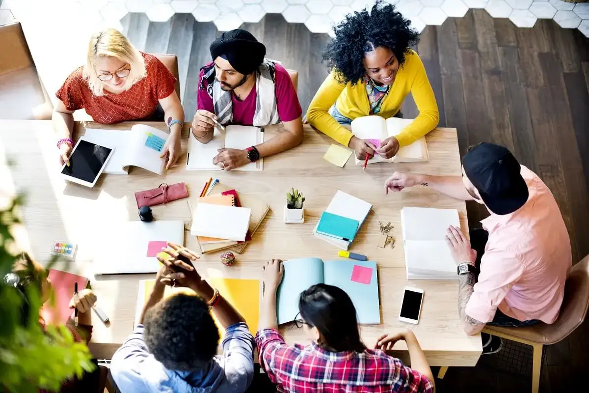 Diverse group collaborating on an emotional intelligence presentation, with books, tablets, and notes spread across a table.