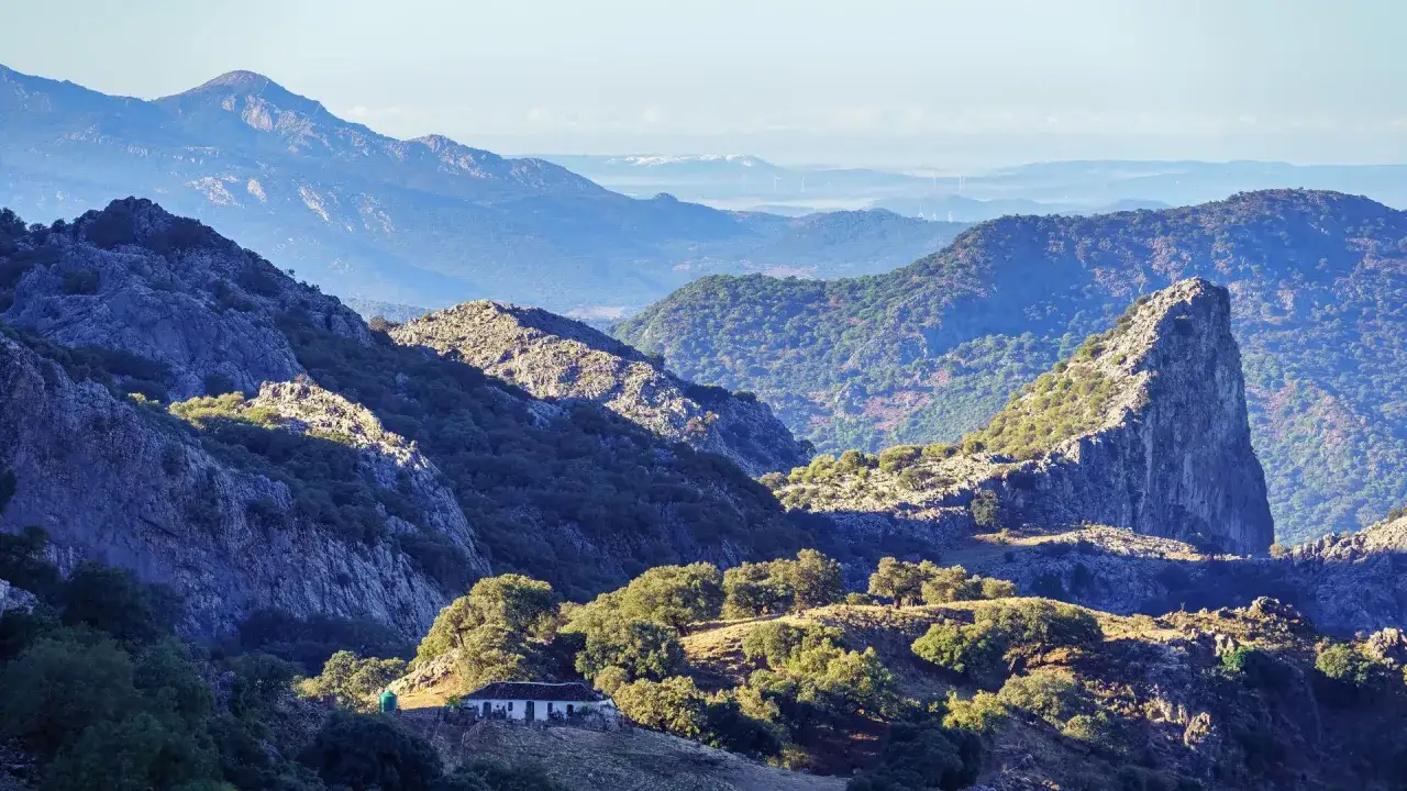 Majestuosa sierra de Cádiz con un pico rocoso y una casa blanca entre encinas.
