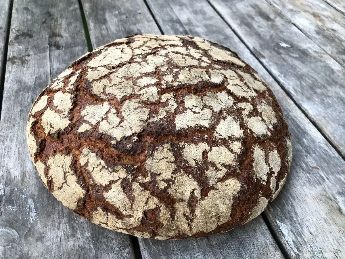Ein frisch gebackenes Dinkelbrot mit knuspriger Kruste liegt auf einer Holzplatte.