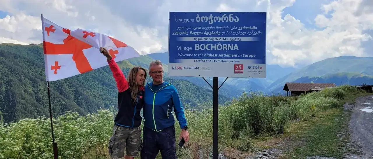 Para zwiedza Gruzję, trzymając flagę. Tablica informuje: 