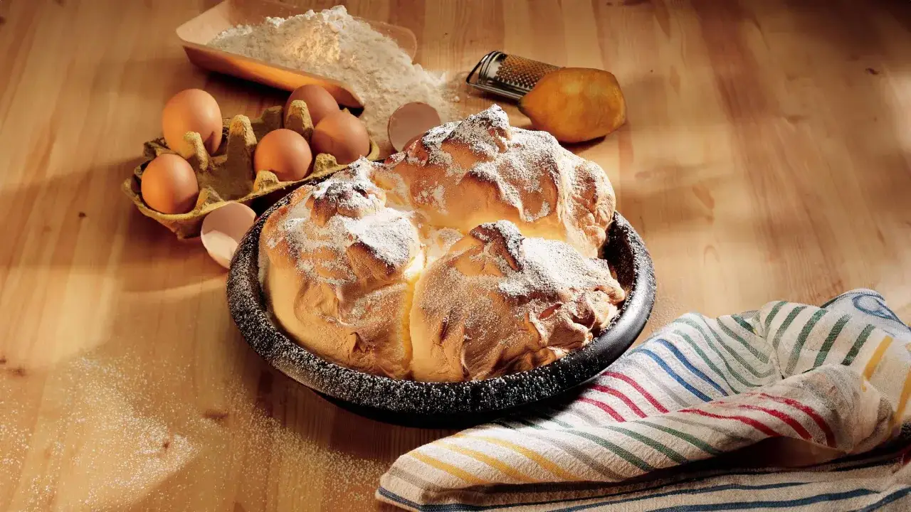 Ein frisch gebackener Salzburger Nockerl, bestäubt mit Puderzucker, neben Eiern, Mehl und einer Zitrone.