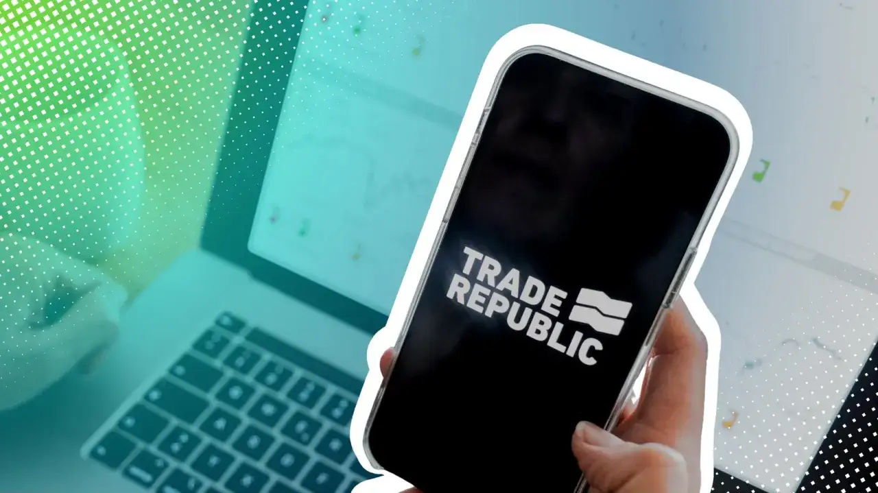 Hand h&auml;lt Smartphone mit Trade Republic Logo. Im Hintergrund Laptop mit Charts, was auf die Trade Republic Einlagensicherung und Investitionen hinweist.
