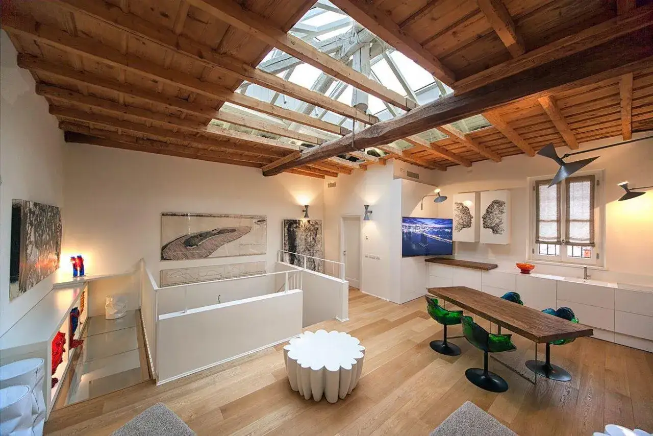 Luminosa mansarda con travi a vista e lucernario. Arredamento moderno con tavolo da pranzo, divani e opere d'arte.