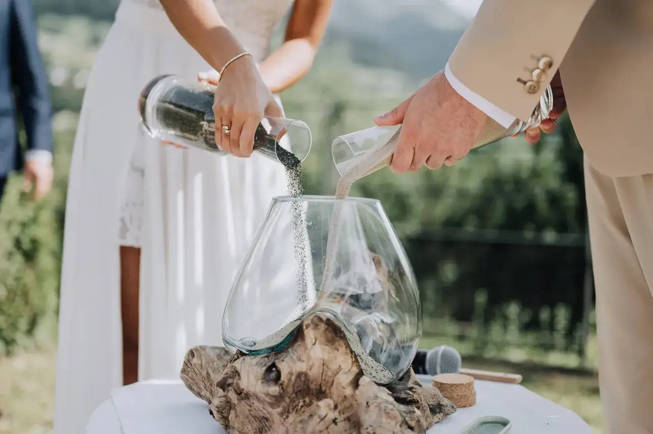 Un couple r&eacute;alise la c&eacute;r&eacute;monie du sable, m&eacute;langeant leurs sables individuels dans un vase pour symboliser leur union.