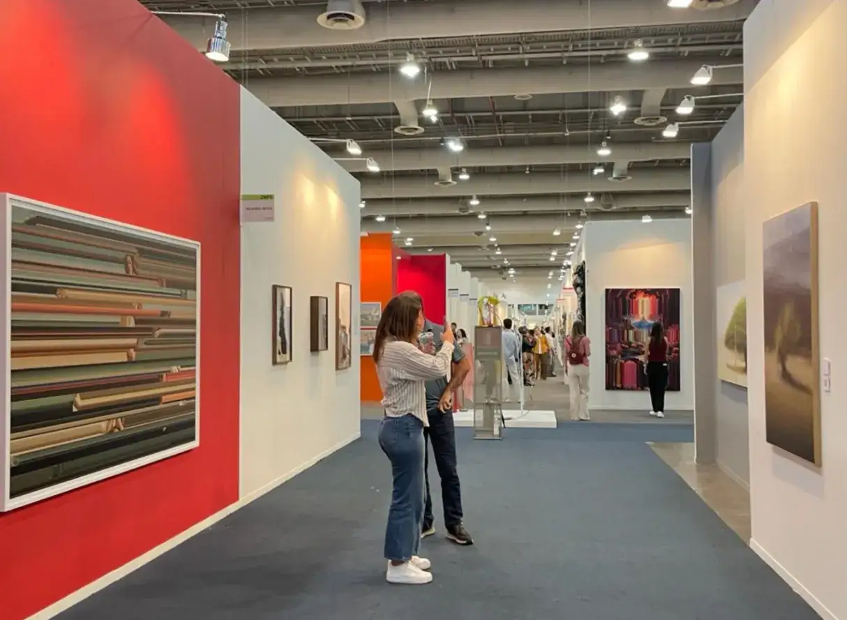 Visitors admire art at the Mexico City Art Fair. A woman takes a photo of a colorful abstract painting.