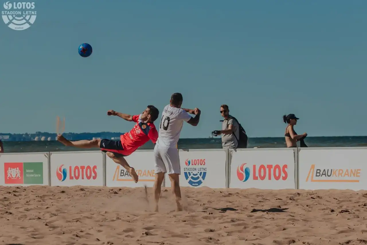 Piłkarz w czerwonej koszulce wykonuje przewrotkę na plaży podczas meczu, kt&oacute;ry może być częścią mistrzostw świata 2024.