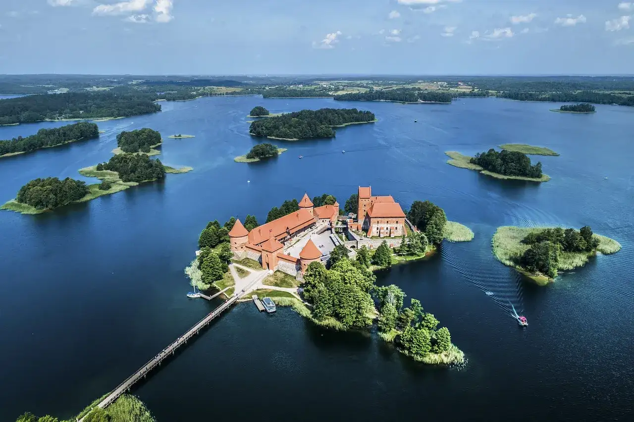Malowniczy zamek na wyspie, połączony mostem z lądem. Wokół jezioro z licznymi wysepkami, tworzące piękne **Trakai atrakcje**.