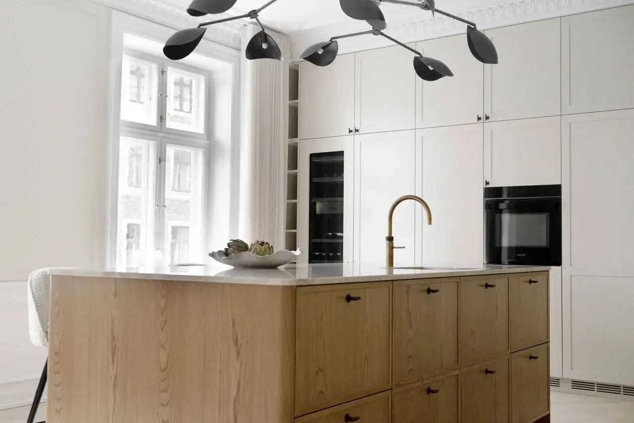 Modernt kök med köksö i trä och marmor, inspirerat av art deco Stockholm. Vinkyl och ugn integrerade i vita skåp.