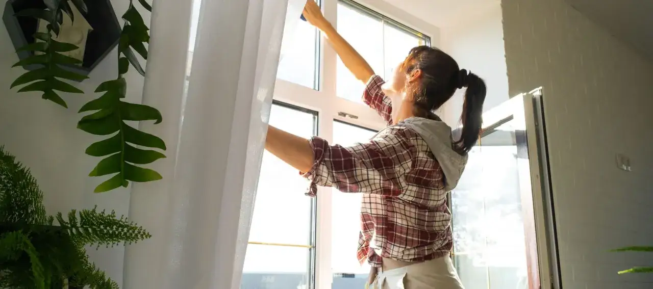 Frau putzt Fenster, damit sie ohne Schlieren strahlen. Sonnenschein und Pflanzen im Hintergrund.