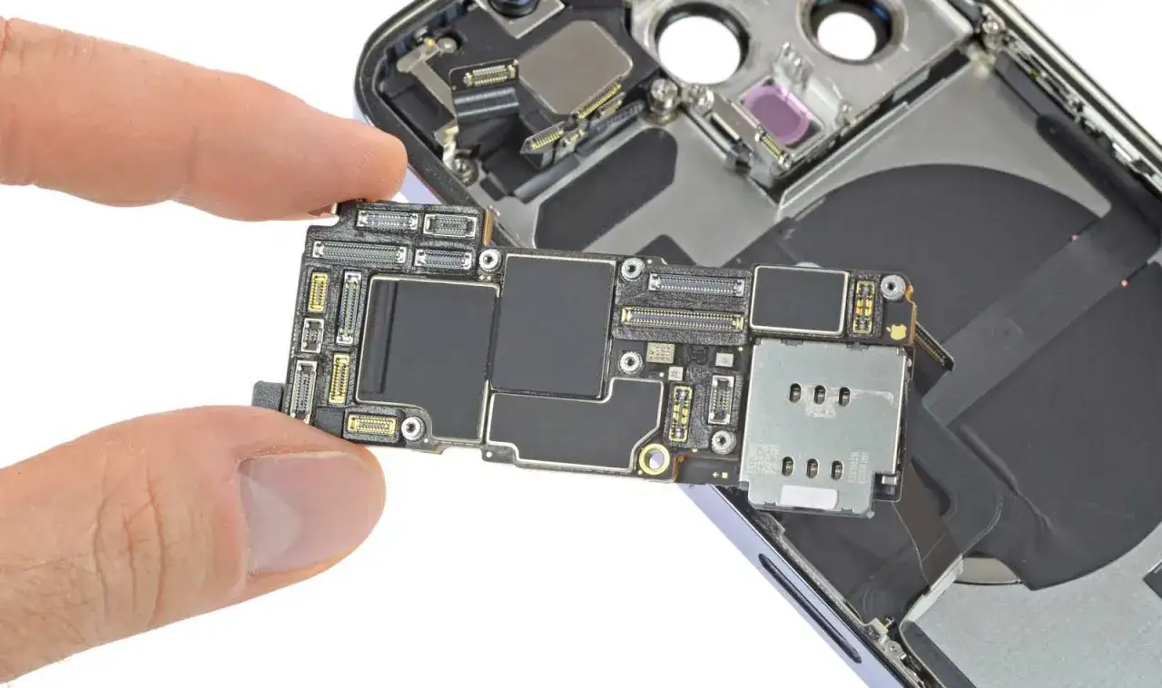 Dłoń trzyma płytę gł&oacute;wną iPhone'a 14, widoczne są czarne układy, w tym pamięć RAM.