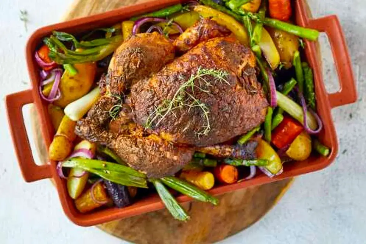 Poulet rôti doré et juteux, servi avec un accompagnement de légumes rôtis colorés : pommes de terre, carottes, asperges et oignons rouges.
