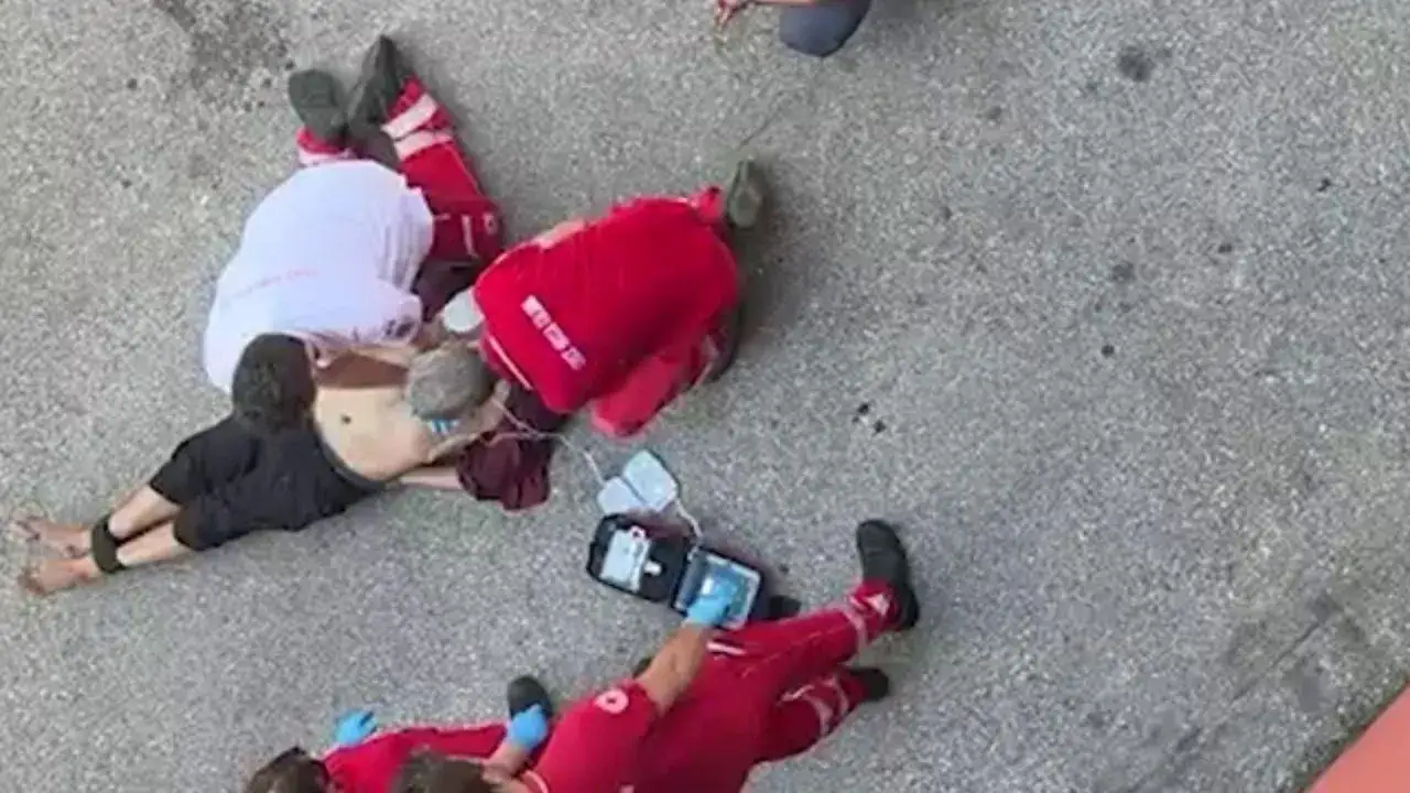 Soccorritori in divisa rossa prestano aiuto a una persona a terra, con le gambe bloccate. Un defibrillatore è pronto all'uso.