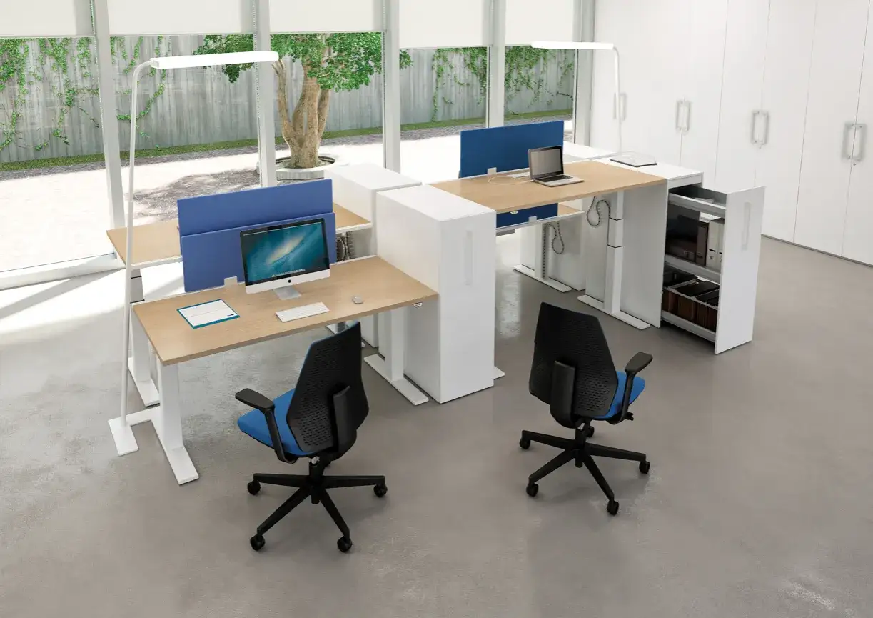 Postes de travail modernes avec écrans, lampes et chaises bleues. L'ergonomie et la prévention TMS sont au cœur de cet aménagement de bureau lumineux.