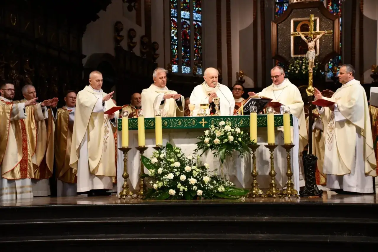 Kapłani w szatach liturgicznych, jak alter Christus, celebrują mszę przy ołtarzu ozdobionym kwiatami i świecami.