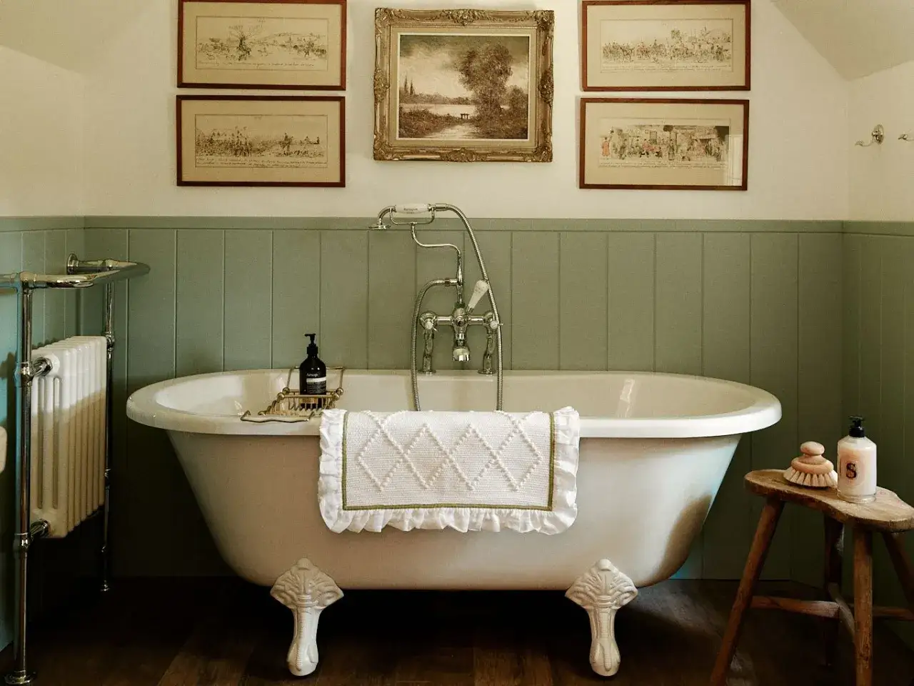 Bagno in stile cottage core con vasca freestanding, stampe d'epoca e dettagli in legno.
