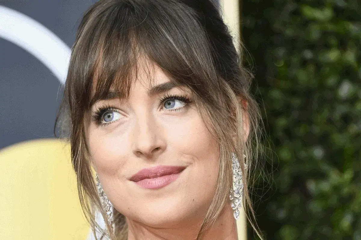 Dakota Johnson z subtelną francuską grzywką i błękitnymi oczami, w długich, błyszczących kolczykach.
