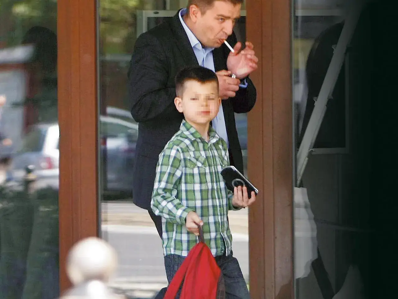 Bartosz Arłukowicz z dziećmi wychodzi z budynku. Chłopiec w kratkę trzyma telefon, mężczyzna pali papierosa.