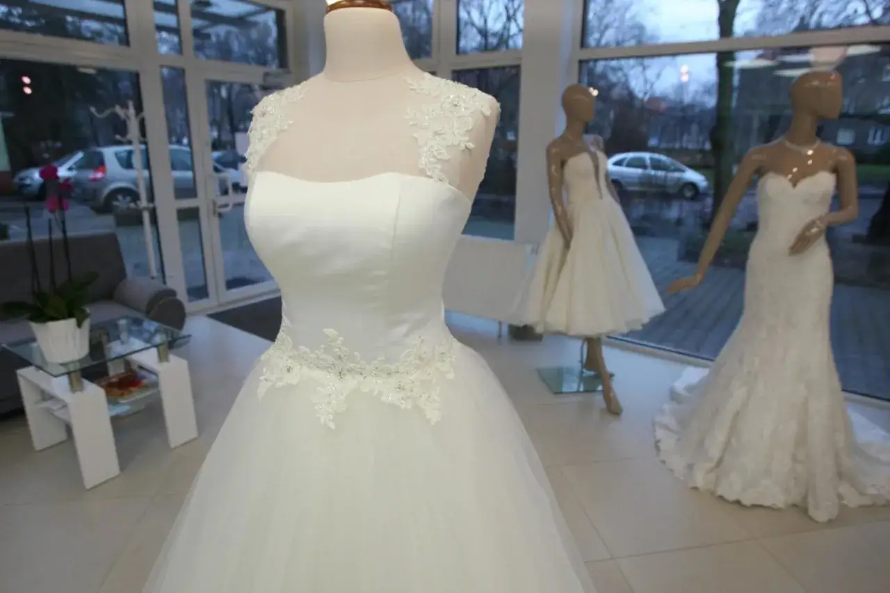Wnętrze eleganckiego komisu sukien ślubnych w Warszawie, w tle wiszące suknie