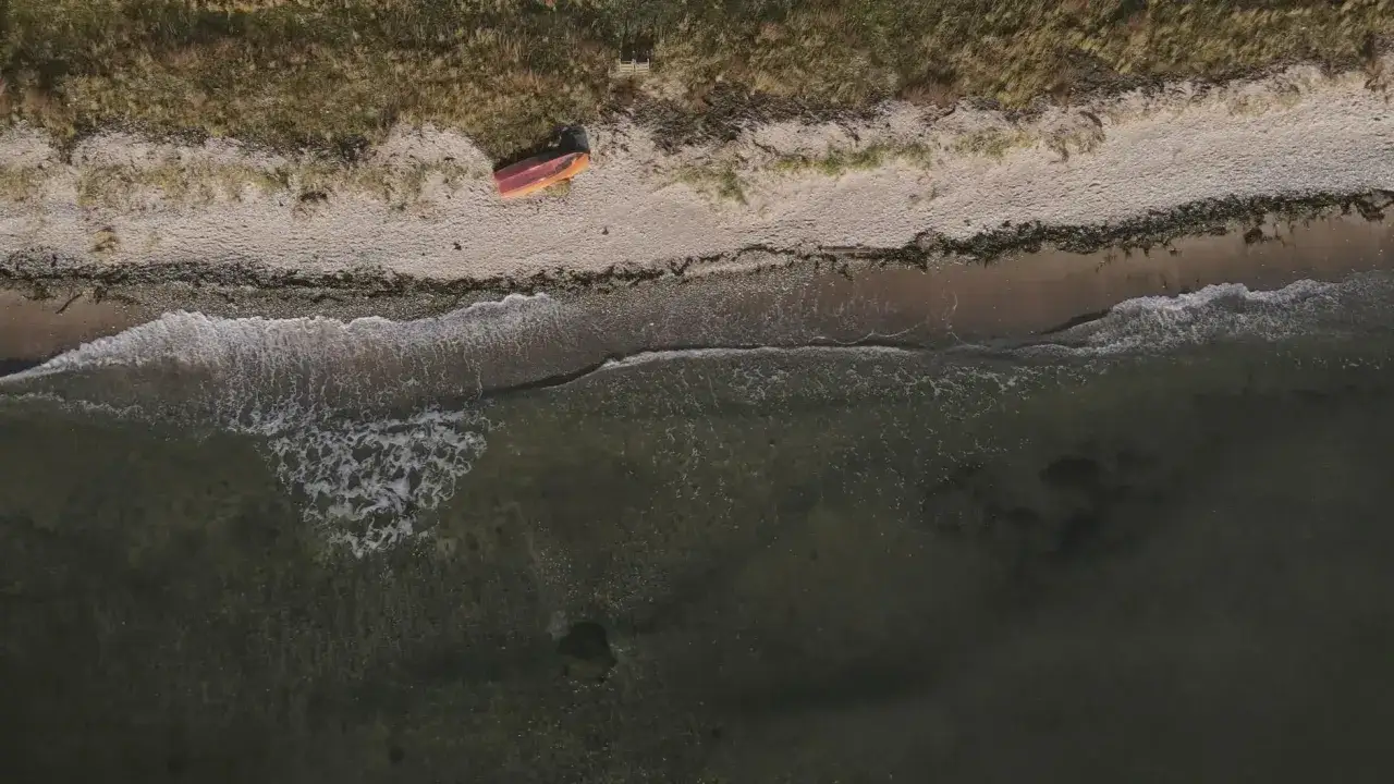 Pomarańczowa łódka na piaszczystej plaży w Szwecji, z falami obmywającymi brzeg.