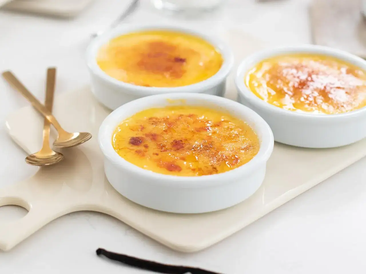 Trois ramequins de cr&egrave;me br&ucirc;l&eacute;e, parfaits pour une recette de cr&egrave;me br&ucirc;l&eacute;e facile et rapide. Des cuill&egrave;res dor&eacute;es sont pos&eacute;es &agrave; c&ocirc;t&eacute;.