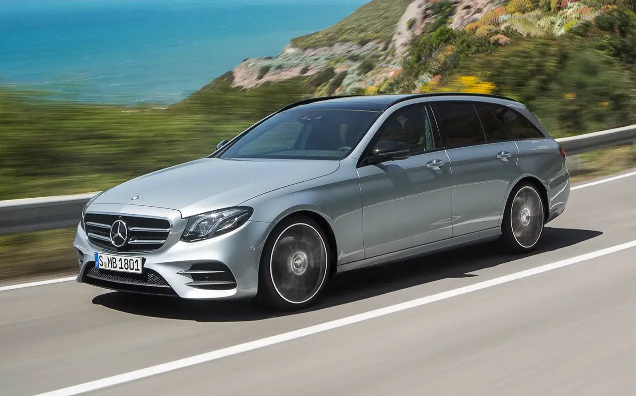 Srebrny Mercedes E300de kombi pędzi po krętej drodze nad morzem.