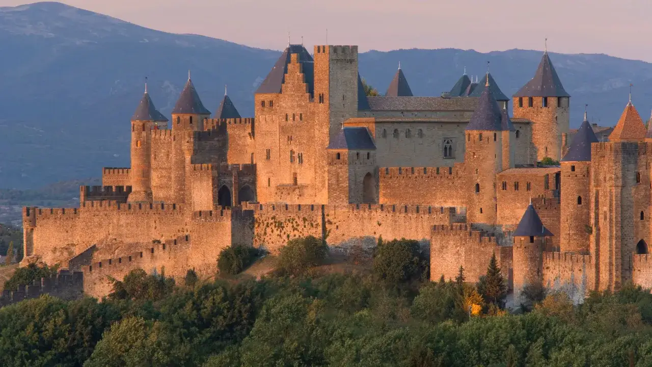 La Cité de Carcassonne, un des plus célèbres châteaux en France, se dresse majestueusement au coucher du soleil, ses remparts dorés se détachant sur les collines bleutées.