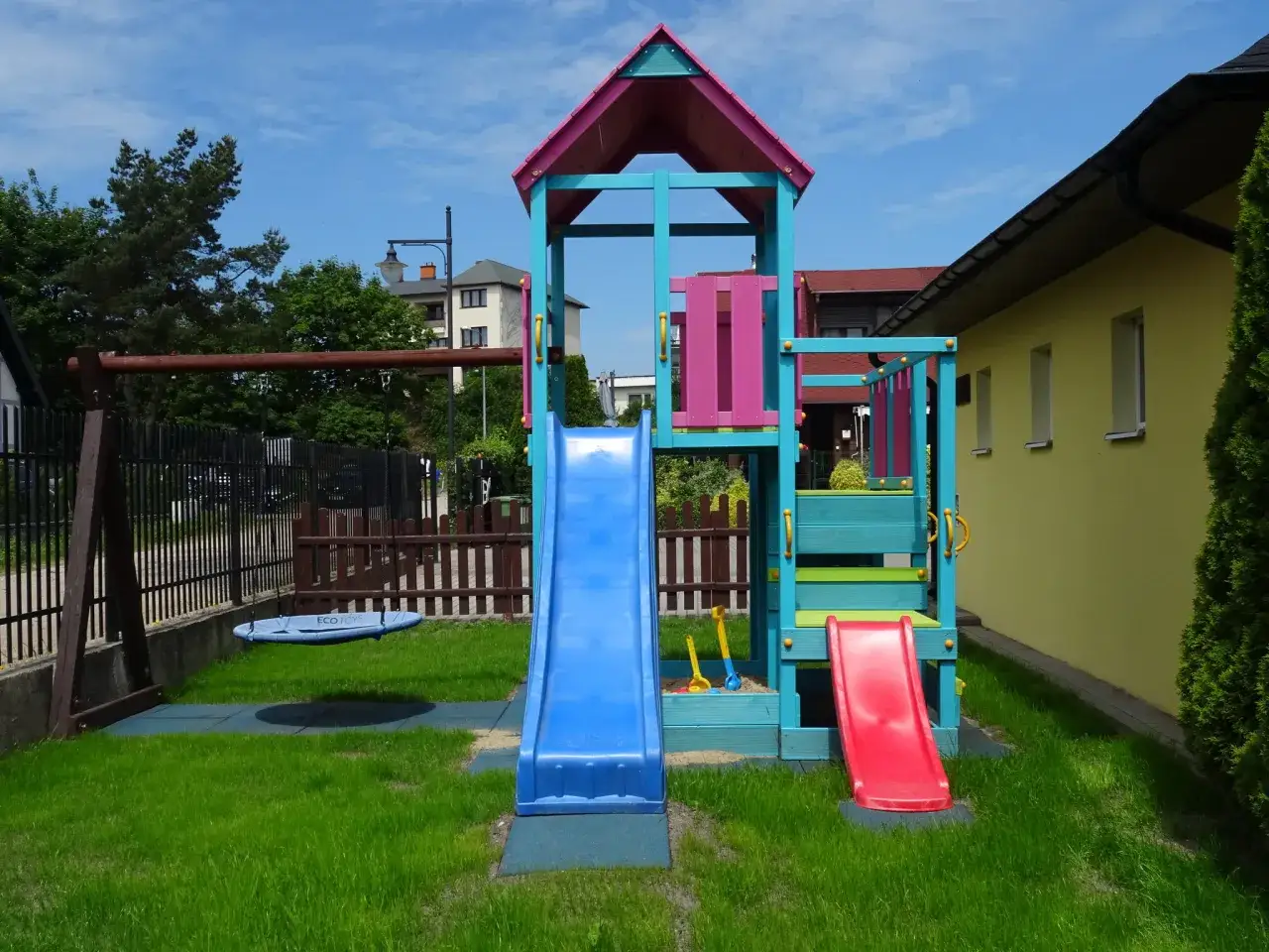 Kolorowy plac zabaw z huśtawką i zjeżdżalniami, idealny dla dzieci wypoczywających w Willa Global Jastrzębia Góra.