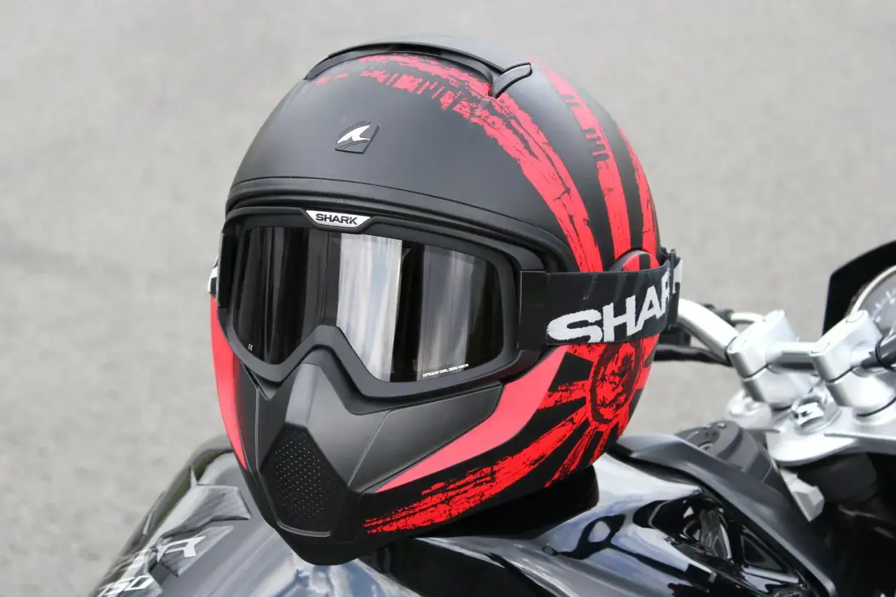 Casco da moto Shark nero e rosso, stile aggressivo, con maschera integrata. Pu&ograve; essere jet o integrale, pronto per l'avventura.