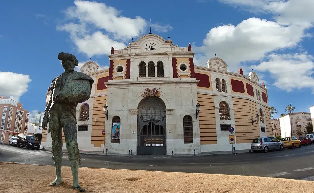 Estatua de un torero frente a la Plaza de Toros de Almería, con un cielo azul y nubes blancas.