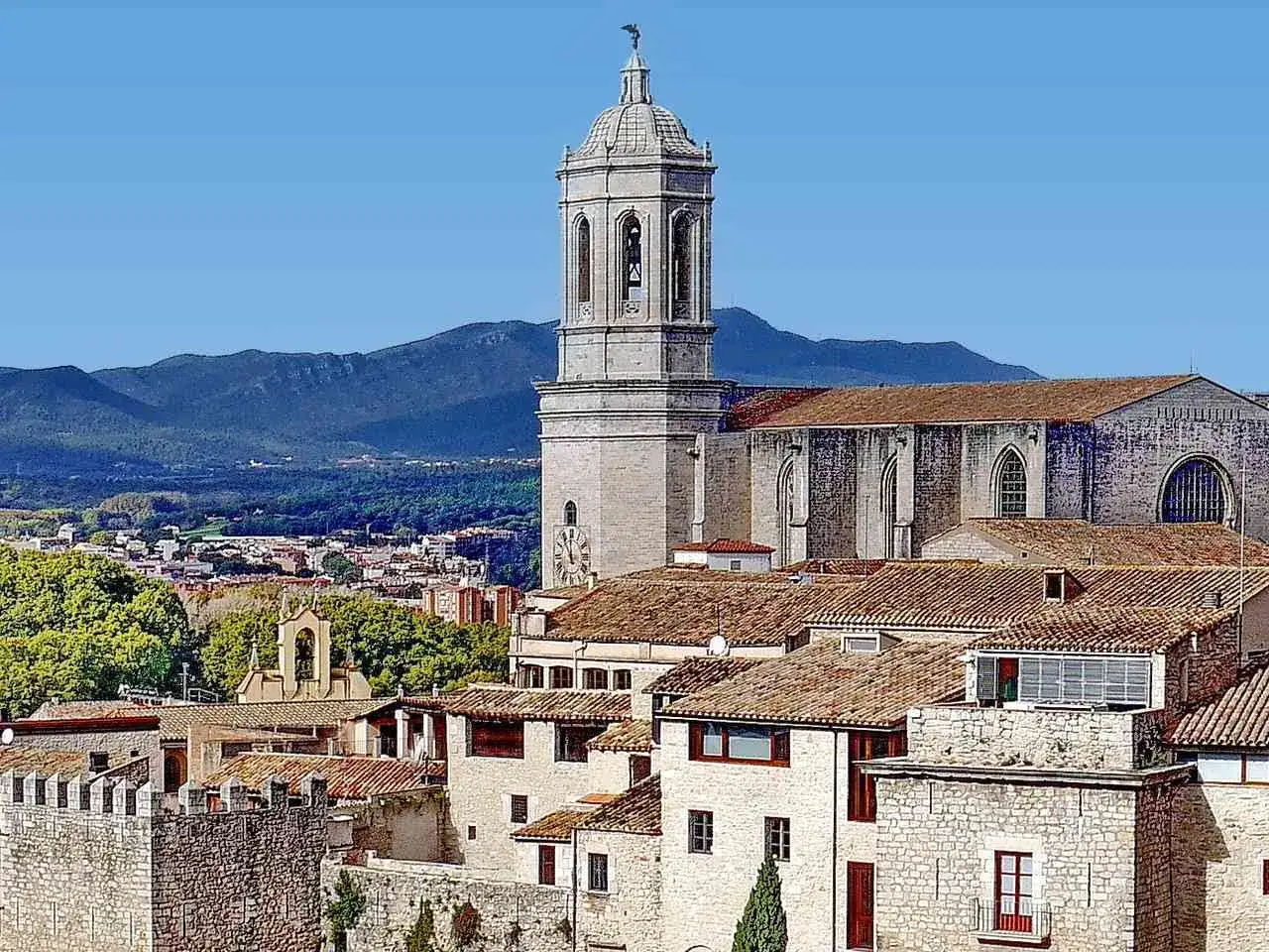 Blick über die Dächer von Girona, Spanien, mit dem markanten Glockenturm der Kathedrale und den Bergen im Hintergrund.