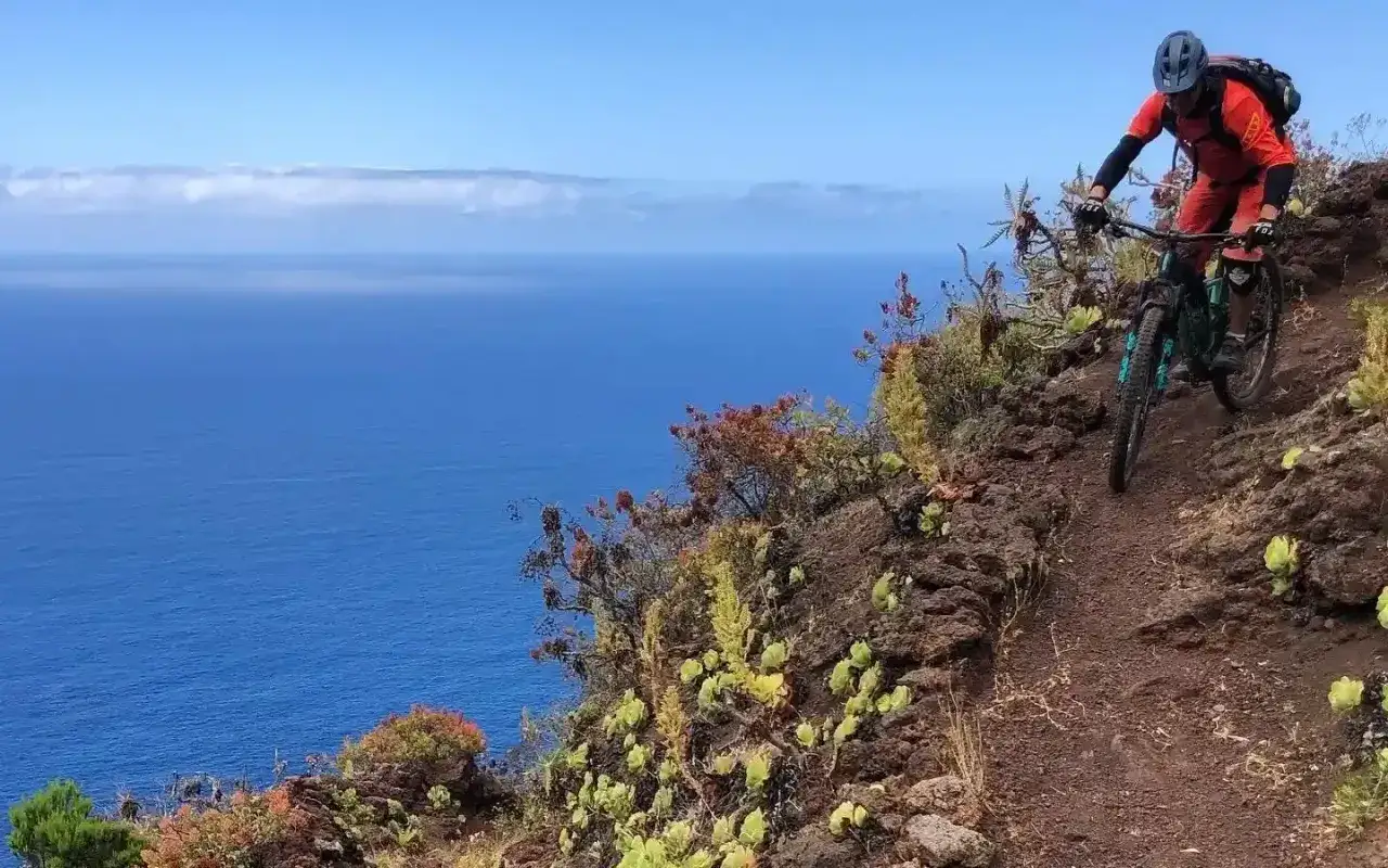 Ciclista desciende por un sendero rocoso con vistas al océano azul. ¡Increíbles rutas en bici Gran Canaria!