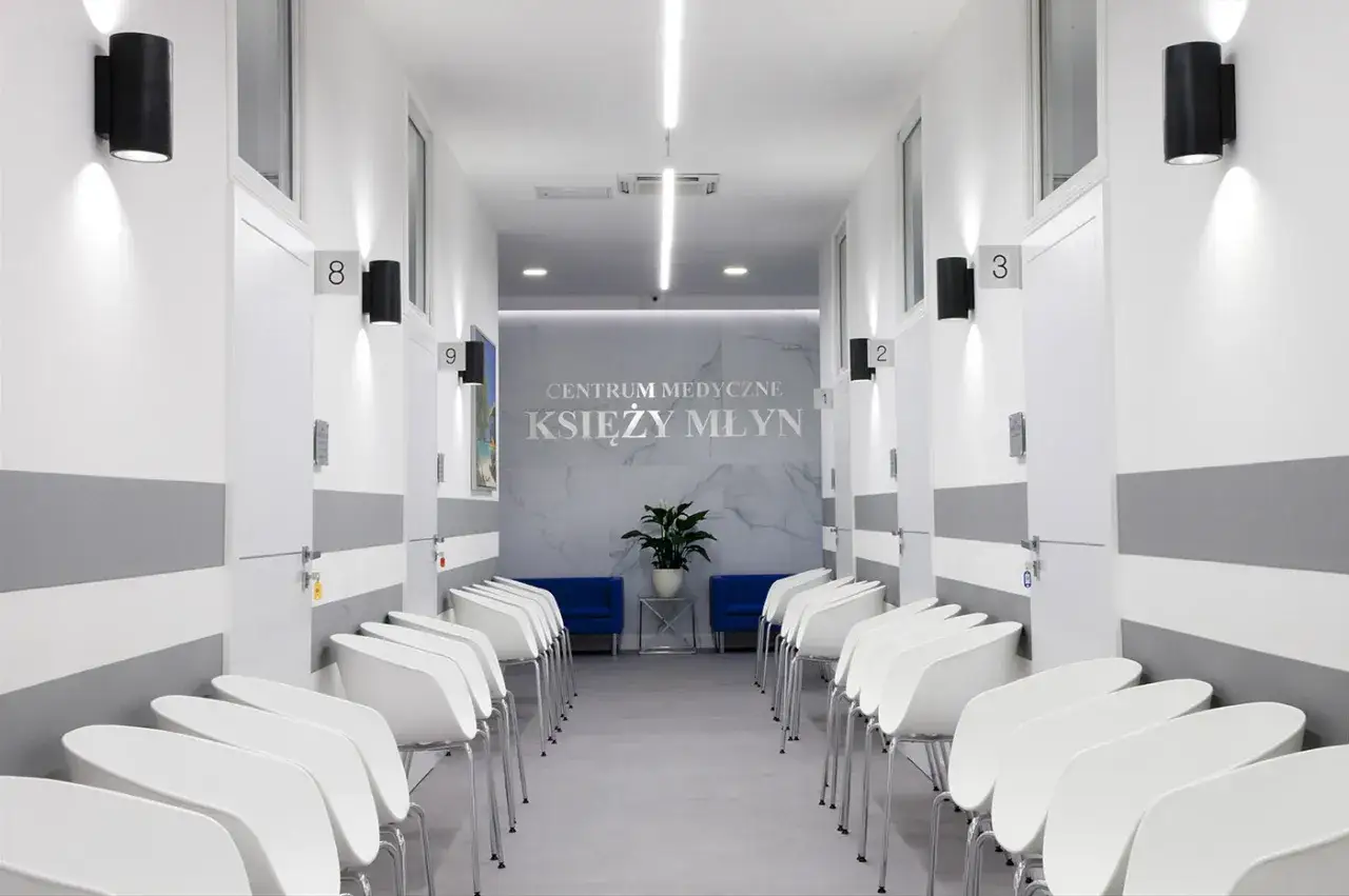 Nowoczesny korytarz centrum medycznego z białymi drzwiami, numerami, czarnymi lampami i rzędami białych krzeseł.