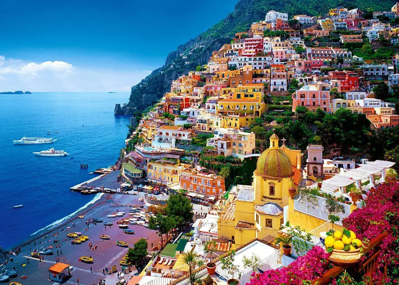 Positano, gdzie kręcono bez litości 3, z kolorowymi domami na zboczu góry, plażą i błękitnym morzem.